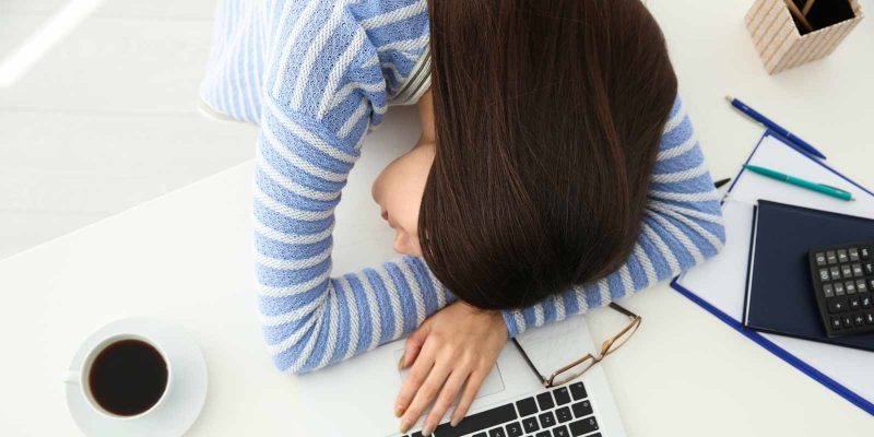 Young woman with head on desk feeling burned out